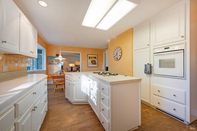 kitchen featuring kitchen peninsula, white cabinets, light hardwood / wood-style floors, decorative light fixtures, and white appliances