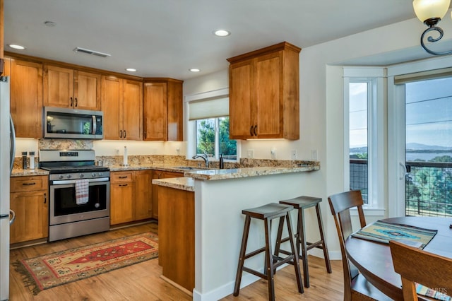 kitchen featuring light hardwood / wood-style flooring, kitchen peninsula, sink, light stone countertops, and appliances with stainless steel finishes