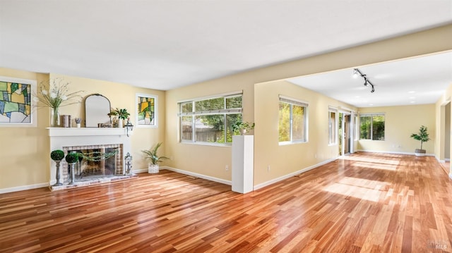 unfurnished living room featuring light wood-type flooring, a brick fireplace, a healthy amount of sunlight, and track lighting