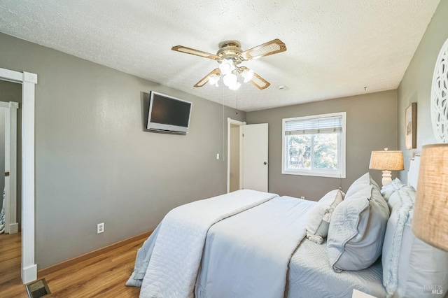 bedroom with a ceiling fan, a textured ceiling, visible vents, and wood finished floors