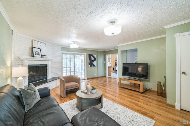 living area featuring a textured ceiling, ornamental molding, a brick fireplace, and wood finished floors