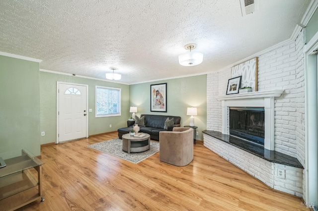 living room featuring a textured ceiling, a fireplace, wood finished floors, visible vents, and ornamental molding