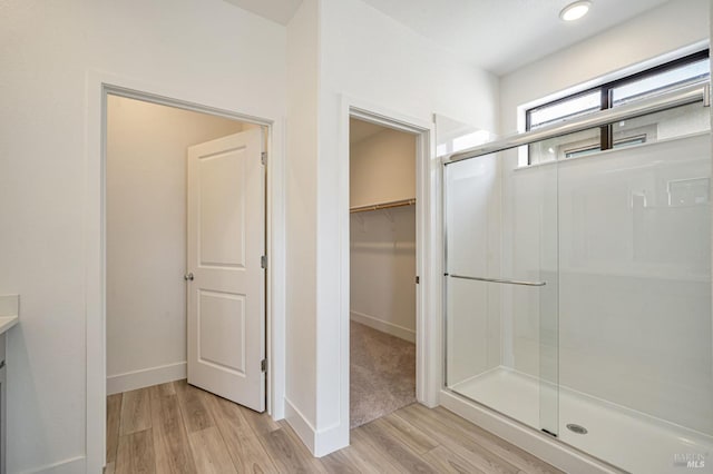 full bath with a shower stall, a spacious closet, wood finished floors, and baseboards