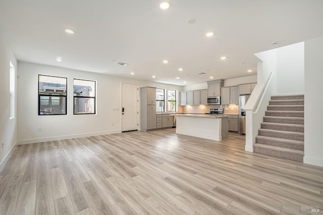 unfurnished living room featuring visible vents, baseboards, recessed lighting, stairs, and light wood-type flooring