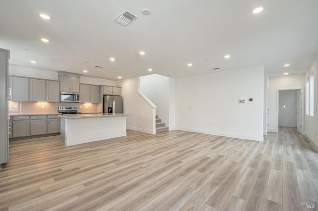 kitchen featuring visible vents, a center island, open floor plan, gray cabinets, and appliances with stainless steel finishes