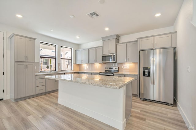 kitchen featuring visible vents, a kitchen island, gray cabinetry, decorative backsplash, and appliances with stainless steel finishes