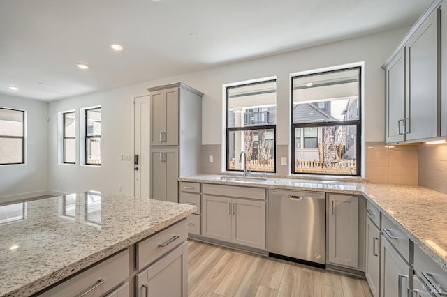 kitchen featuring tasteful backsplash, light wood finished floors, gray cabinetry, stainless steel dishwasher, and a sink