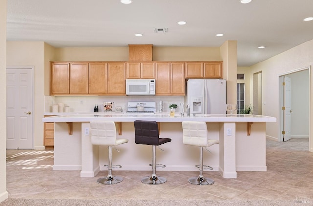 kitchen featuring a center island with sink, a breakfast bar area, light tile patterned flooring, light brown cabinetry, and white appliances