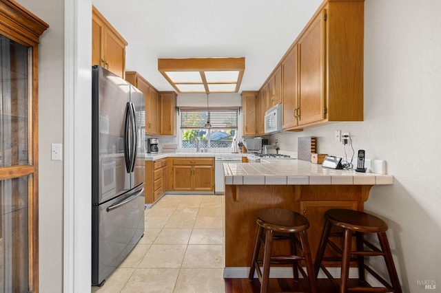 kitchen featuring light tile patterned floors, tile countertops, a kitchen bar, kitchen peninsula, and white appliances