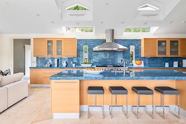 kitchen featuring wall chimney exhaust hood, tasteful backsplash, light brown cabinetry, and a high ceiling