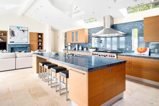 kitchen with a large island with sink, wall chimney range hood, sink, backsplash, and a kitchen breakfast bar