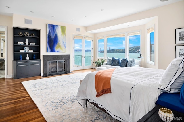 bedroom with access to exterior, dark wood-type flooring, a water view, and french doors