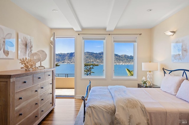 bedroom featuring beam ceiling, multiple windows, a water view, and light wood-type flooring