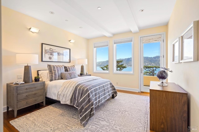 bedroom with beamed ceiling, hardwood / wood-style floors, and access to outside