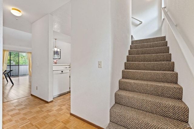 staircase featuring parquet flooring, sink, and an inviting chandelier