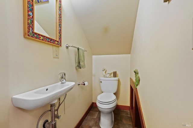 half bath with lofted ceiling, a sink, toilet, and baseboards