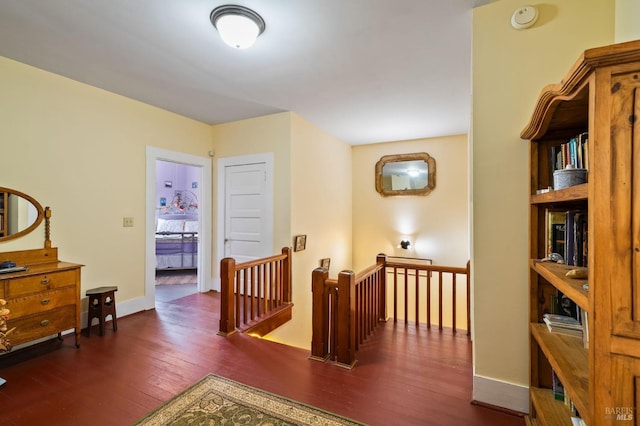 hallway with dark wood-type flooring, an upstairs landing, and baseboards