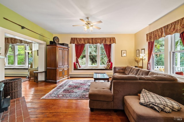 living area with a healthy amount of sunlight, dark wood finished floors, baseboard heating, and ceiling fan