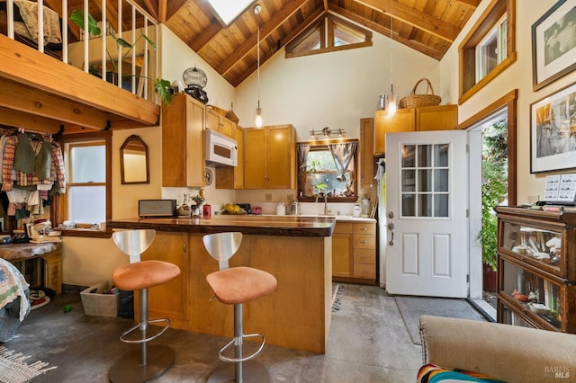 kitchen featuring a skylight, white microwave, a sink, wooden ceiling, and a kitchen bar