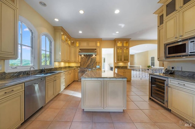 kitchen with stainless steel appliances, a center island, sink, wall chimney range hood, and beverage cooler