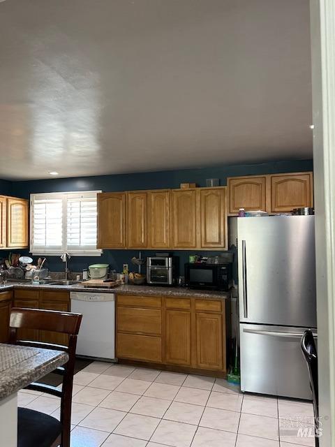 kitchen featuring sink, light tile patterned flooring, dishwasher, and stainless steel refrigerator