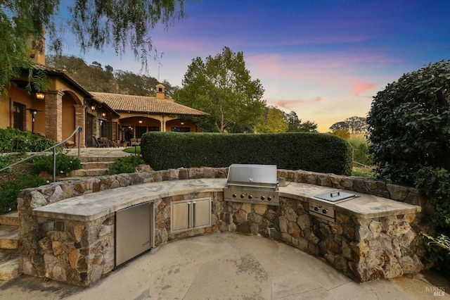 patio terrace at dusk with area for grilling and exterior kitchen