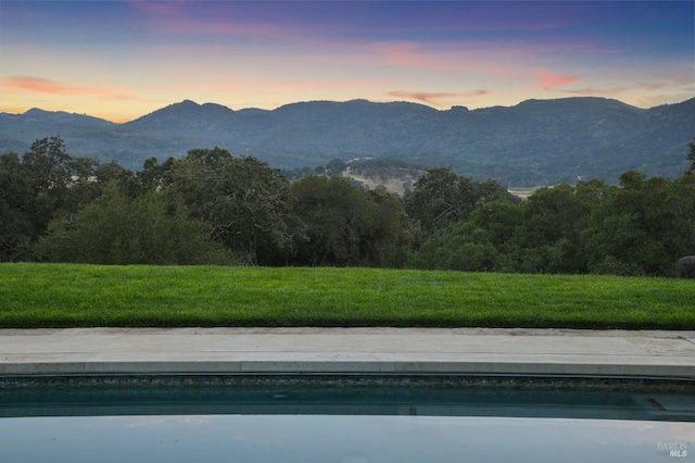 pool at dusk featuring a yard and a mountain view