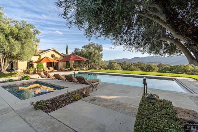 view of pool with a hot tub, a mountain view, and a patio area