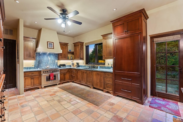 kitchen featuring decorative backsplash, stainless steel range, custom range hood, sink, and ceiling fan