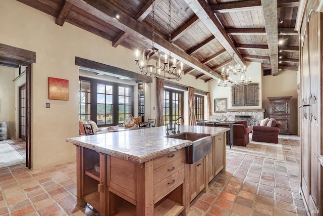 kitchen with sink, french doors, beamed ceiling, pendant lighting, and a kitchen island with sink