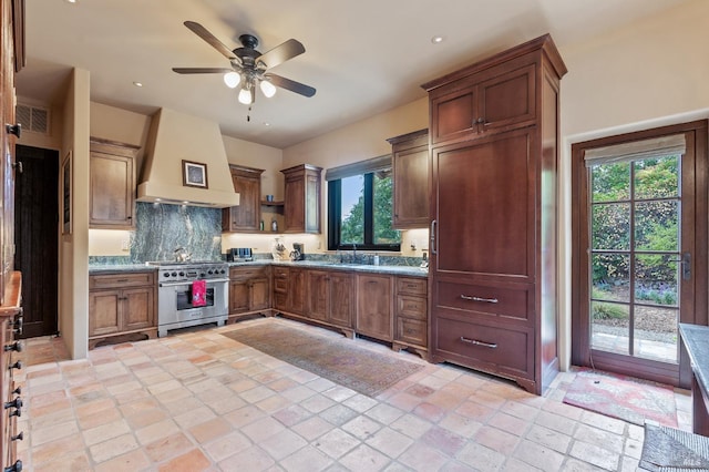 kitchen with backsplash, ceiling fan, stainless steel range, custom range hood, and light stone counters