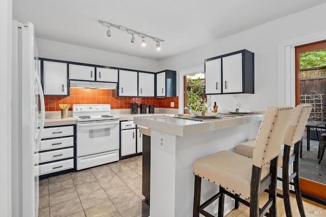 kitchen featuring kitchen peninsula, white cabinets, backsplash, a breakfast bar, and white appliances