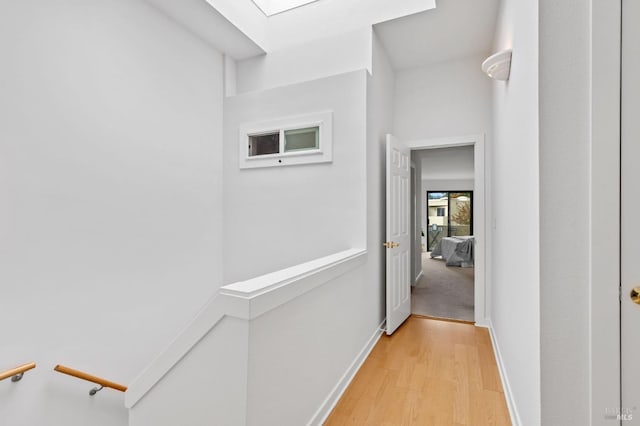 corridor with light wood finished floors, baseboards, and an upstairs landing