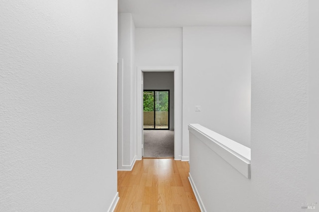 corridor with baseboards, an upstairs landing, and light wood-type flooring
