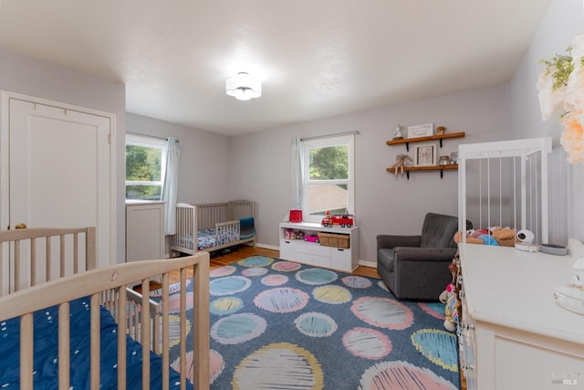 bedroom with hardwood / wood-style flooring, multiple windows, and a nursery area