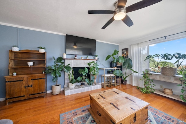 living room with light wood-type flooring, a tiled fireplace, ceiling fan, and crown molding