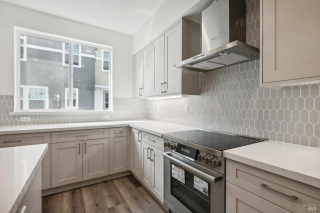 kitchen with dark wood-type flooring, electric stove, wall chimney range hood, light countertops, and tasteful backsplash