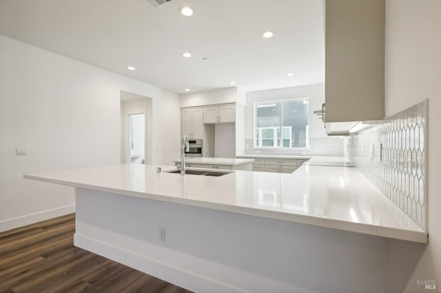 kitchen featuring baseboards, decorative backsplash, dark wood-style flooring, a peninsula, and a sink