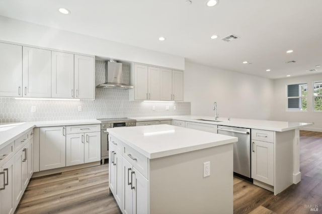 kitchen featuring stainless steel appliances, a peninsula, a sink, visible vents, and wall chimney range hood