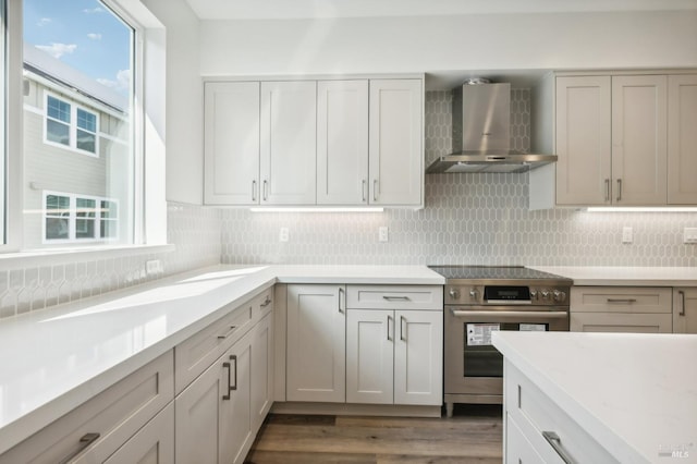 kitchen featuring dark wood-type flooring, white cabinets, decorative backsplash, stainless steel range, and wall chimney range hood