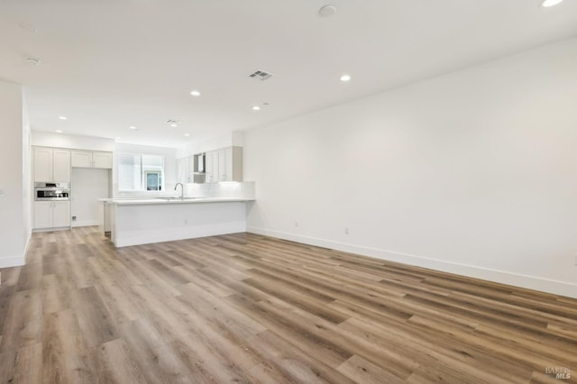 unfurnished living room featuring recessed lighting, visible vents, a sink, light wood-type flooring, and baseboards