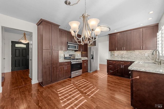 kitchen with sink, appliances with stainless steel finishes, hanging light fixtures, a chandelier, and dark wood-type flooring