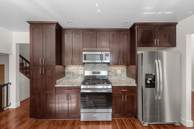 kitchen with appliances with stainless steel finishes, tasteful backsplash, light stone countertops, dark brown cabinets, and dark hardwood / wood-style flooring