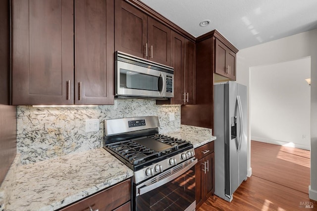 kitchen with stainless steel appliances, light hardwood / wood-style floors, light stone counters, decorative backsplash, and dark brown cabinetry