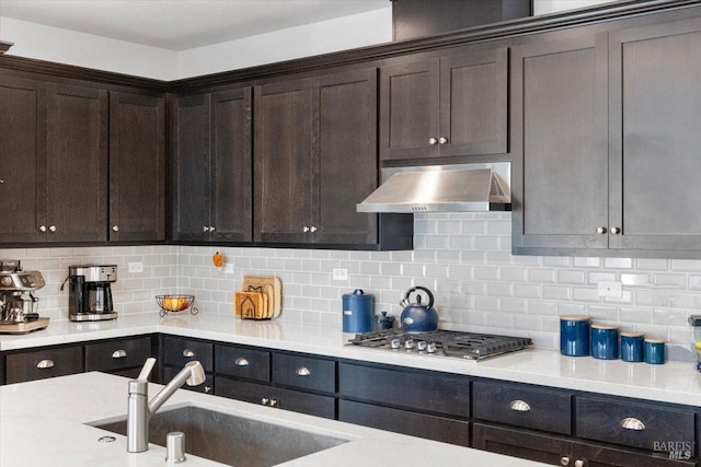 kitchen with decorative backsplash, sink, exhaust hood, and dark brown cabinets