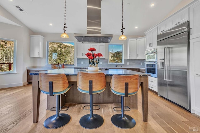 kitchen with island range hood, a kitchen island, appliances with stainless steel finishes, and decorative light fixtures