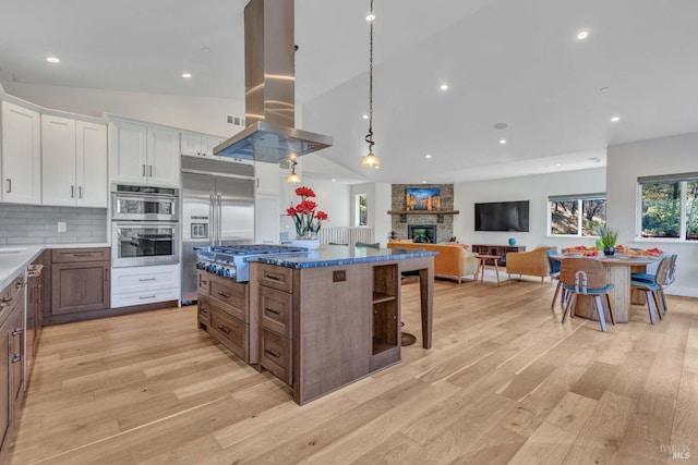 kitchen with white cabinets, appliances with stainless steel finishes, island exhaust hood, a fireplace, and pendant lighting