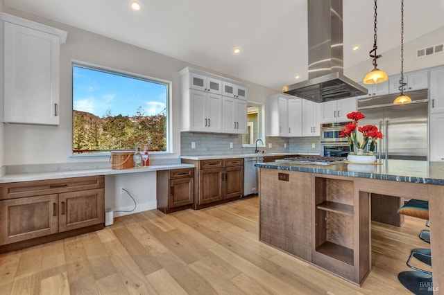 kitchen featuring island range hood, visible vents, appliances with stainless steel finishes, glass insert cabinets, and pendant lighting