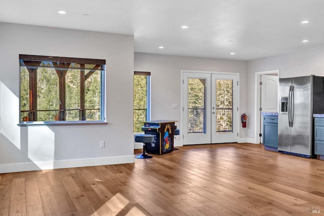 unfurnished living room with a healthy amount of sunlight, light wood-style flooring, and french doors