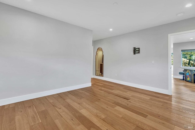 spare room with light wood-style flooring, baseboards, arched walkways, and recessed lighting